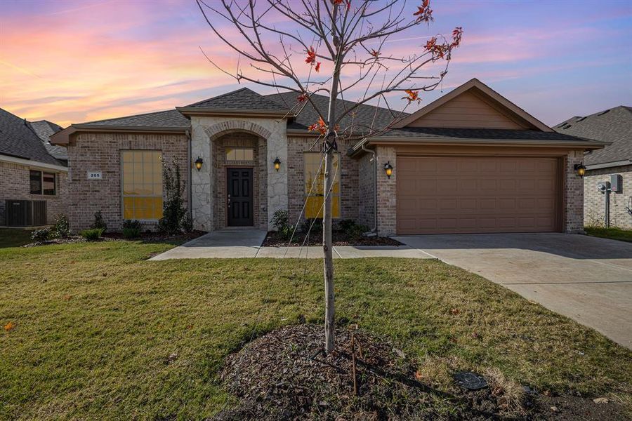 View of front of house with a garage, central AC unit, and a lawn