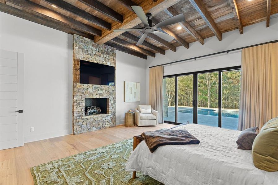 Bedroom featuring a wooden ceiling with exposed beams, access to exterior, a stone fireplace, wood finished floors, and a ceiling fan