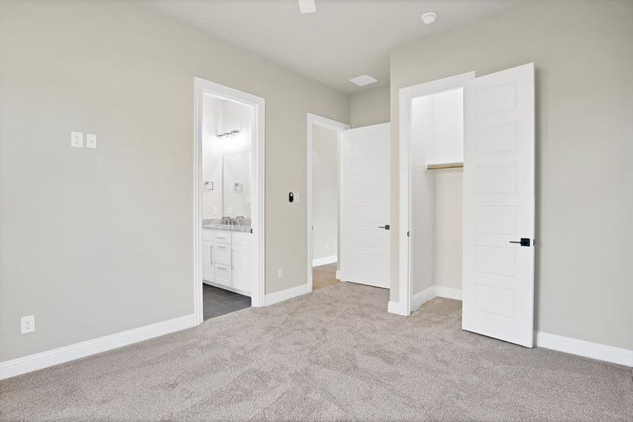 Unfurnished bedroom with ceiling fan, carpet, a closet, a spacious closet, and ensuite bath