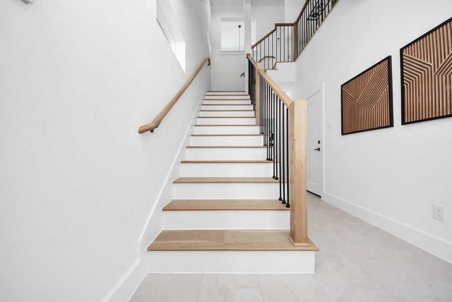 Ascend this modern staircase with light wood steps and sleek black metal railings, set against bright white walls. Geometric wall art adds a contemporary touch, creating an inviting transition between the home’s levels while highlighting its clean, modern design. Ascend this modern staircase with light wood steps and sleek black metal railings, set against bright white walls. Geometric wall art adds a contemporary touch, creating an inviting transition between the home’s levels while highlighting its clean, modern design.