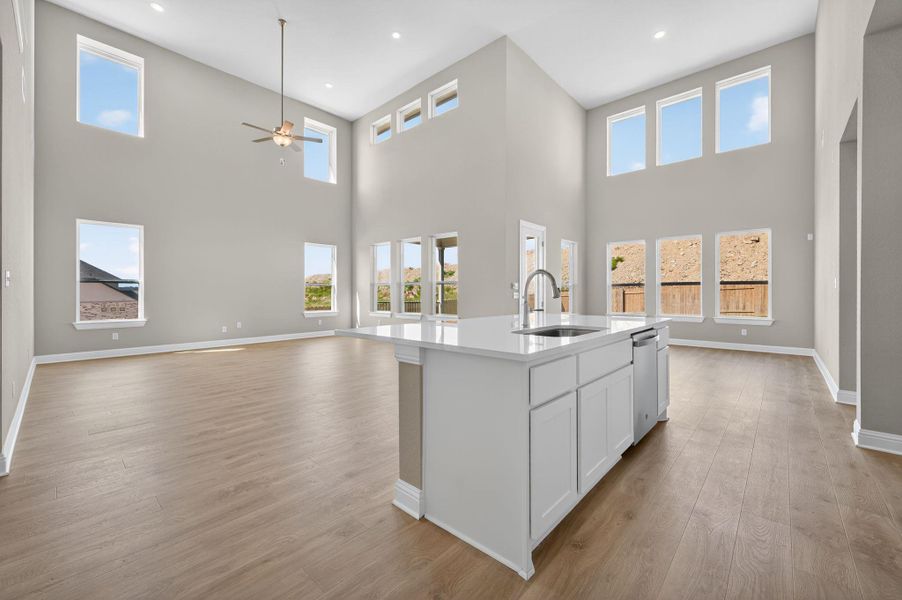 Kitchen with white cabinetry, a high ceiling, light stone countertops, light wood-type flooring, and open floor plan