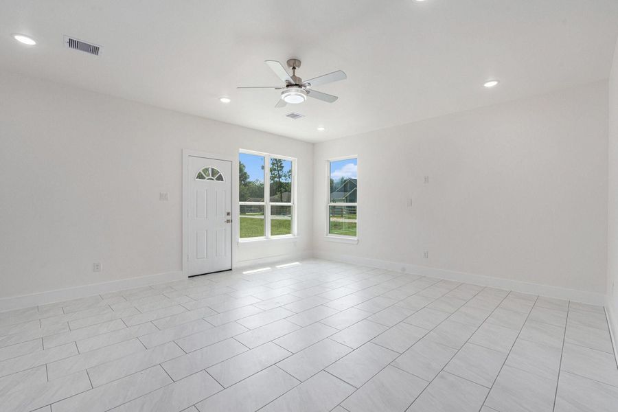 This photo shows a bright, spacious living area with light-colored tile flooring, a ceiling fan, recessed lighting, and large windows providing plenty of natural light. The neutral walls create a clean, modern look. This photo shows a bright, spacious living area with light-colored tile flooring, a ceiling fan, recessed lighting, and large windows providing plenty of natural light. The neutral walls create a clean, modern look.