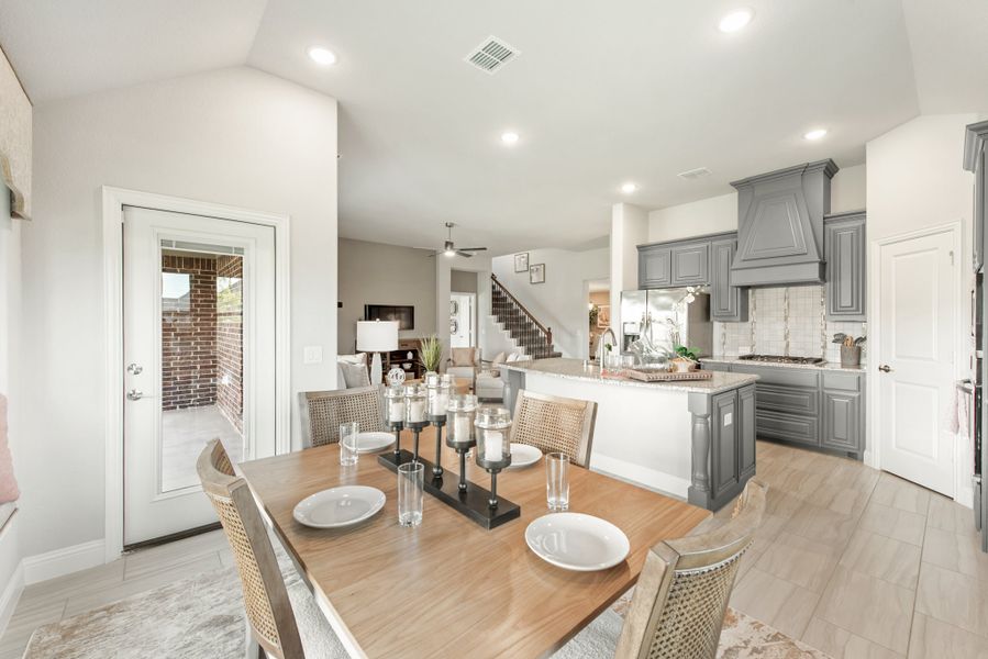 Open-plan dining area with wood table and chairs flowing into kitchen with gray cabinets and large island
