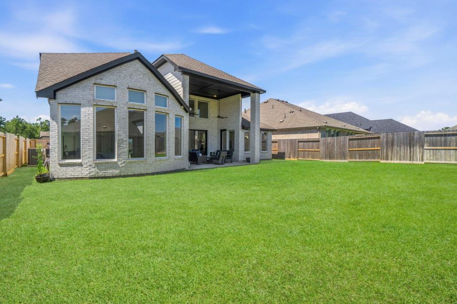 This photo showcases a modern home exterior with a spacious, well-maintained backyard, featuring large windows and a covered patio area, ideal for outdoor activities and relaxation.