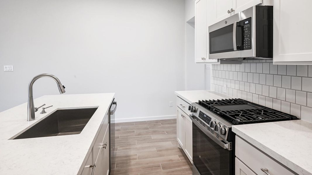 Kitchen with stainless steel appliances, white cabinetry, wood finish floors, light stone counters, and decorative backsplash