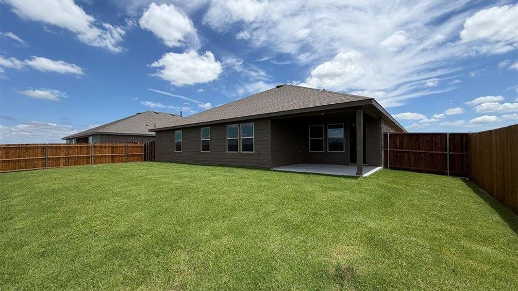 Expansive backyard featuring a manicured lawn, full privacy fencing, and a covered concrete patio