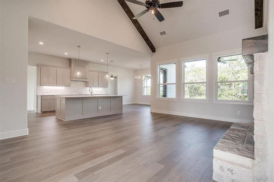 Unfurnished living room featuring ceiling fan with notable chandelier, beam ceiling, high vaulted ceiling, and light hardwood / wood-style flooring