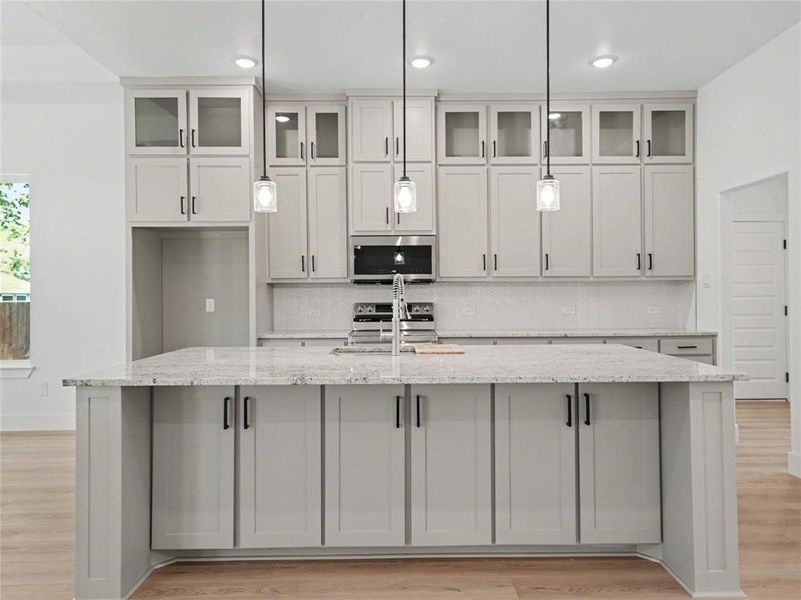 Central kitchen island with a light-toned countertop, shaker-style cabinetry, a built-in sink, and three pendant light fixtures Central kitchen island with a light-toned countertop, shaker-style cabinetry, a built-in sink, and three pendant light fixtures