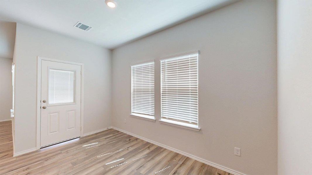 Interior room featuring wood-finish flooring, two windows with blinds, a white door with a glass panel, and light-colored walls Interior room featuring wood-finish flooring, two windows with blinds, a white door with a glass panel, and light-colored walls