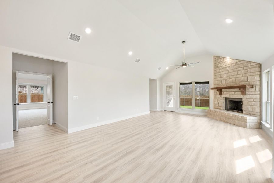 Open living room with vaulted ceiling, stone fireplace, ceiling fan, and light hardwood floors