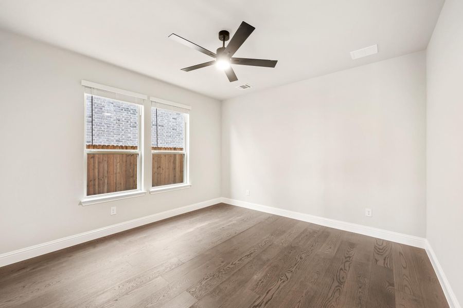 Empty bedroom with hardwood floors, ceiling fan, and two windows with white trim Empty bedroom with hardwood floors, ceiling fan, and two windows with white trim