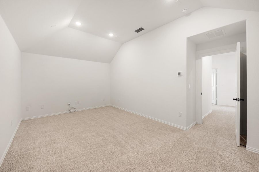 Empty bedroom with vaulted ceiling, beige carpet, white walls, and recessed lighting