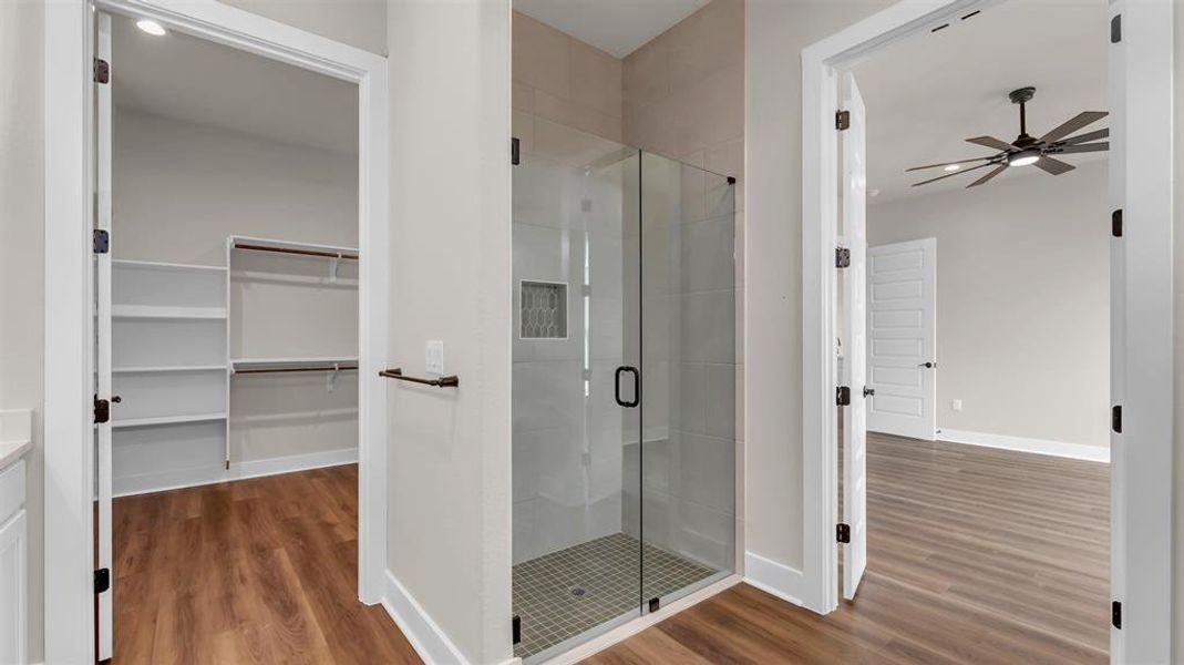 Clean lines and wood-style flooring connect the walk-in closet, glass-enclosed shower, and bedroom. Clean lines and wood-style flooring connect the walk-in closet, glass-enclosed shower, and bedroom.