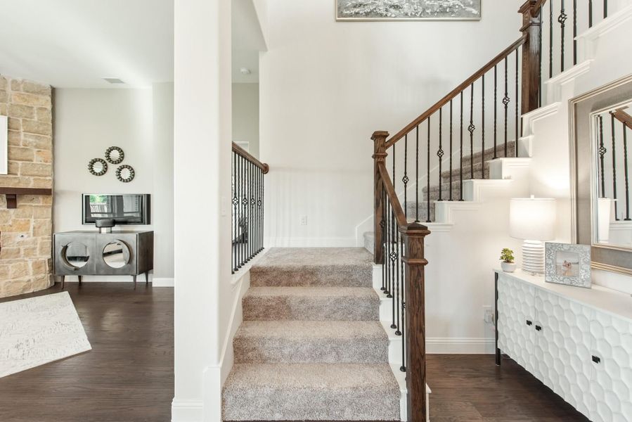Carpeted staircase with wood and iron railing, white walls, and stone fireplace visible in adjacent living room