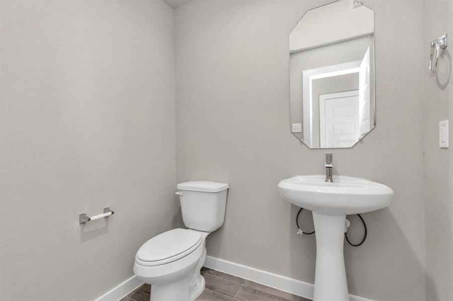 Sophisticated half bathroom adorned with contemporary finishes. The elegant 5-panel door welcomes you to a space where style meets functionality. Notice the sleek hardware accents that add a touch of modern charm. The vanity boasts light-colored countertops, beautifully complemented by a tasteful vanity light, creating a well-lit and inviting atmosphere. Sample photo of completed home with similar floor plan. As built color and selections may vary.