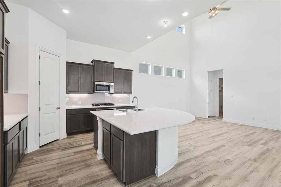 Kitchen featuring light hardwood / wood-style flooring, backsplash, high vaulted ceiling, sink, and a center island with sink