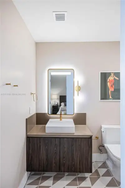 Modern floating vanity featuring wood-finish cabinetry, a white rectangular vessel sink, polished brass hardware, a backlit rectangular mirror, and geometric patterned floor tile