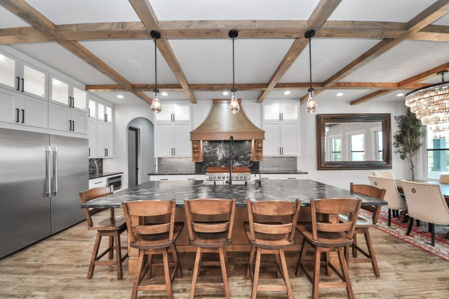 Stunning kitchen with a large marble island, wooden beam ceiling, and elegant pendant lighting. A grand range hood and ample cabinetry provide both style and functionality.