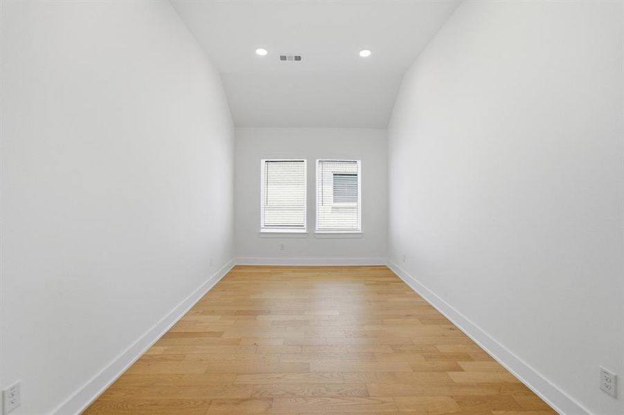Room featuring light wood-finish flooring, white walls, and a vaulted ceiling