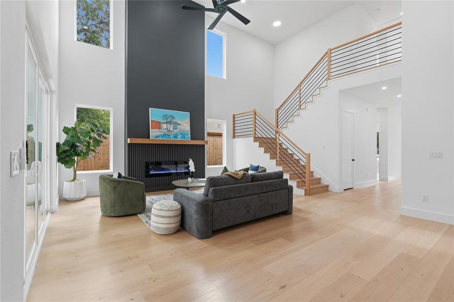 Spacious living area featuring high ceilings, light wood-finish flooring, and a contemporary fireplace with a sleek dark surround and wood mantle Spacious living area featuring high ceilings, light wood-finish flooring, and a contemporary fireplace with a sleek dark surround and wood mantle