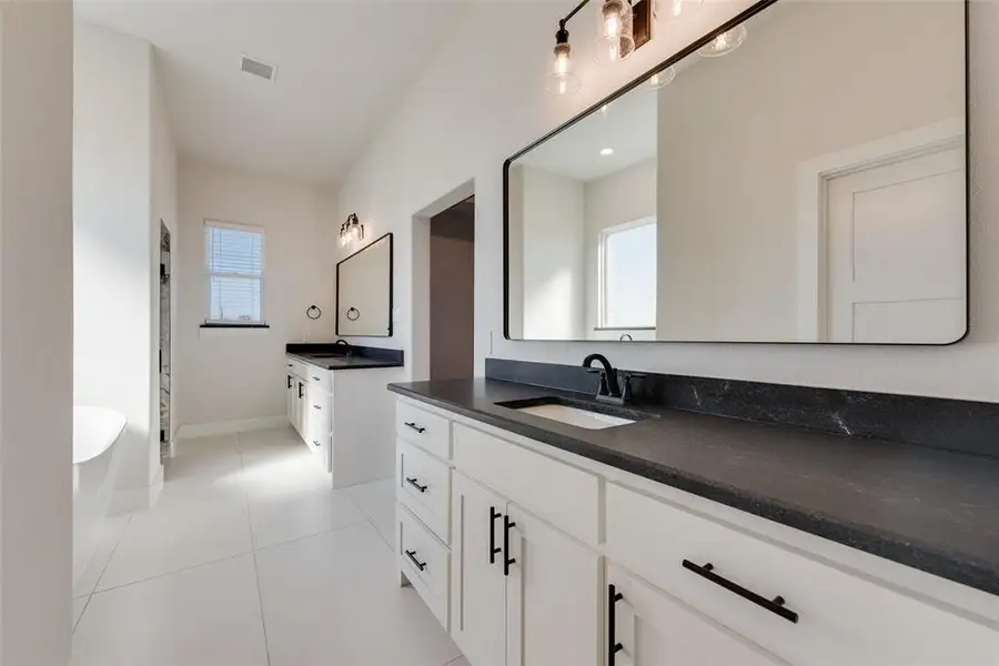 Spacious bathroom featuring dual vanities with dark countertops, white cabinetry, and matte black hardware