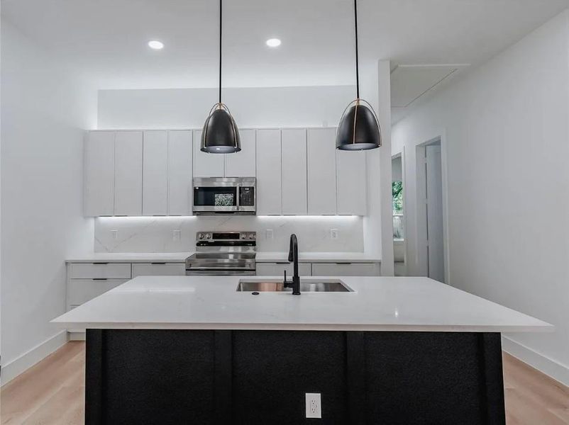 Kitchen with white cabinets, stainless steel appliances, light wood-type flooring, a center island with sink, and decorative light fixtures