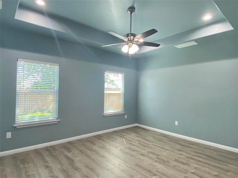 A well-lit bedroom features a tray ceiling with recessed lighting and a ceiling fan, complemented by sleek wood flooring. A well-lit bedroom features a tray ceiling with recessed lighting and a ceiling fan, complemented by sleek wood flooring.