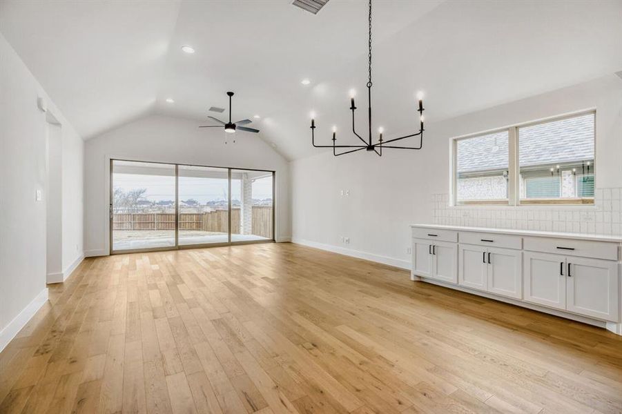 Unfurnished dining area with a chandelier, plenty of natural light, vaulted ceiling, a ceiling fan, and light wood finished floors