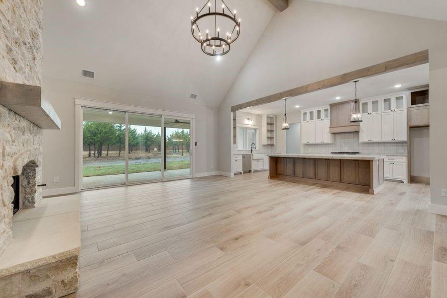 Unfurnished living room with an inviting chandelier, a stone fireplace, light wood-type flooring, and high vaulted ceiling