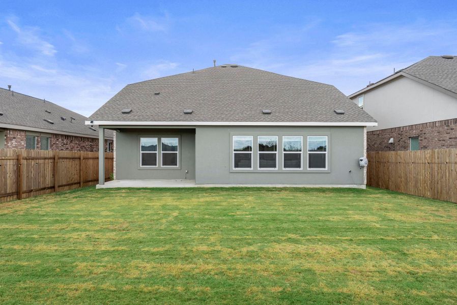 A well-maintained lawn stretches behind a residence featuring a covered patio and multiple windows. A well-maintained lawn stretches behind a residence featuring a covered patio and multiple windows.