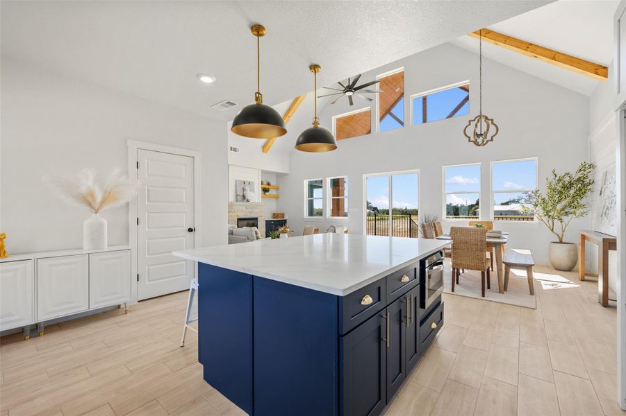 Kitchen featuring high vaulted ceiling, blue cabinetry, pendant lighting, a kitchen island, and light stone countertops