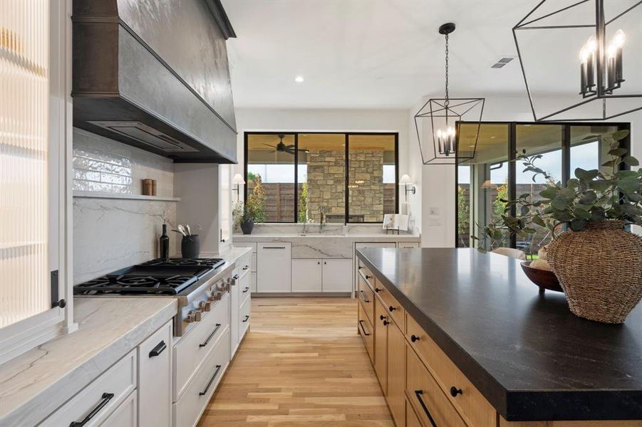 Dual tone kitchen with stainless steel gas cooktop, light wood-style flooring, dark stone countertops, backsplash, and pendant lighting Dual tone kitchen with stainless steel gas cooktop, light wood-style flooring, dark stone countertops, backsplash, and pendant lighting