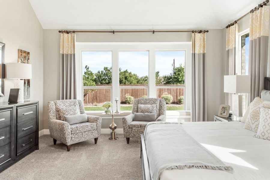 Master bedroom with large windows, two accent chairs, and neutral carpet and gray curtains
