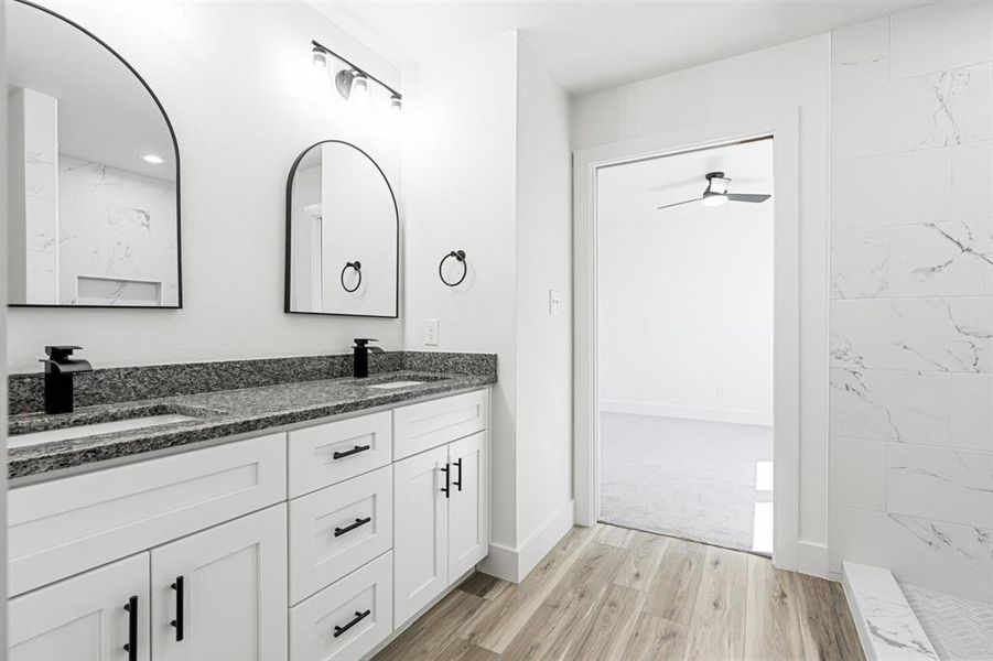 Full bath with double vanity, light wood-style flooring, a marble finish shower, and ceiling fan