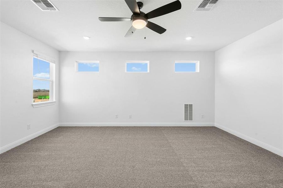 Spacious room featuring neutral carpeting, white walls, multiple windows providing natural light, recessed lighting, and a ceiling fan with integrated illumination