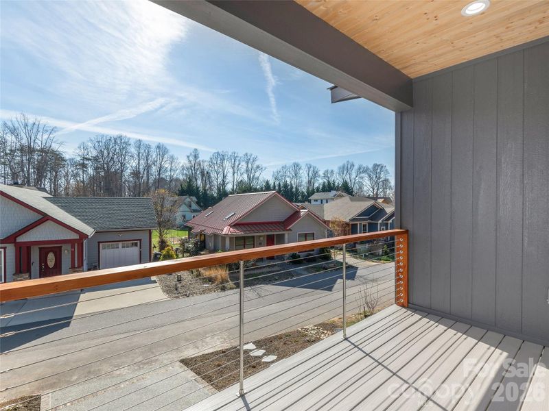 Covered upper-level porch with tongue-and-groove wood ceiling and cable railing, offering a comfortable outdoor living space just off the main level.