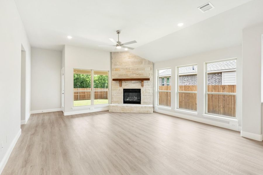 Open living room with stone fireplace, wood mantel, light hardwood floors, and ceiling fan Open living room with stone fireplace, wood mantel, light hardwood floors, and ceiling fan