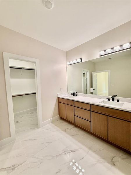 Full bath featuring marble finish flooring, double vanity, baseboards, and a spacious closet