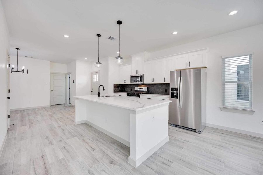 Contemporary kitchen with ample cabinet storage, stainless steel refrigerator, gas range, built-in microwave, and sleek black hardware that adds contrast to the bright white cabinetry.