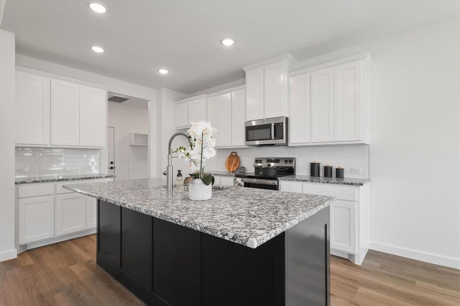 Kitchen with wood-type flooring, white cabinets, a center island with sink, and stainless steel appliances