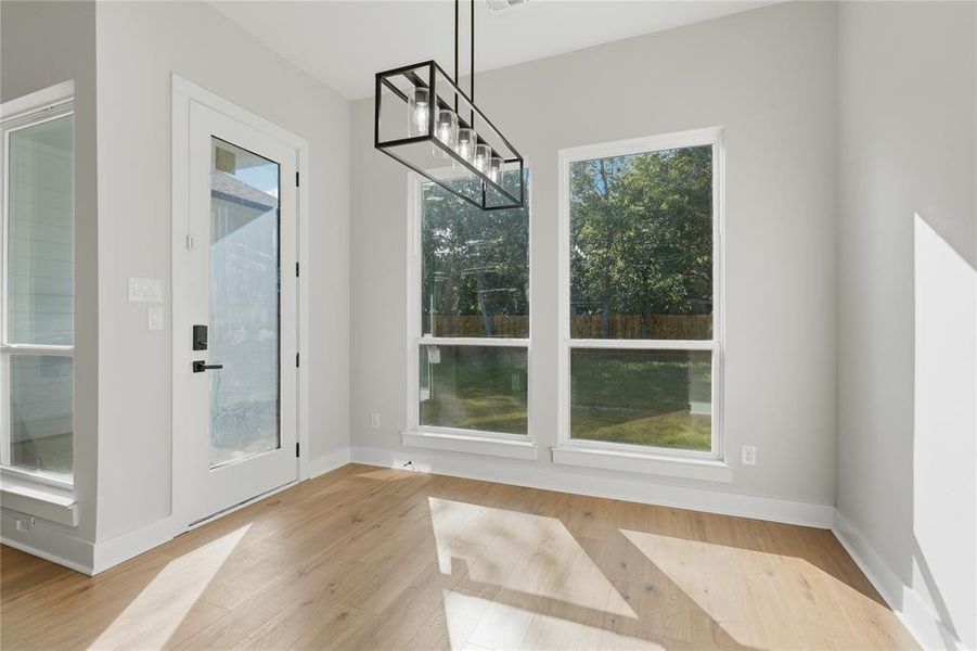 Room featuring wood-finish flooring, a modern linear chandelier, and a full-light exterior door Room featuring wood-finish flooring, a modern linear chandelier, and a full-light exterior door