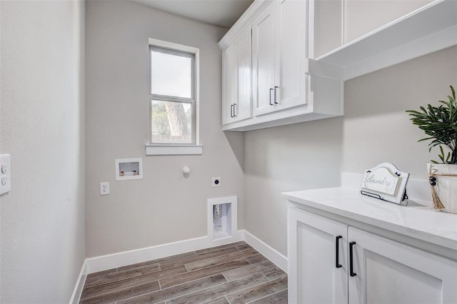 Laundry area featuring electric dryer hookup, cabinet space, wood look finish tiled floors, washer and dryer hookups,
