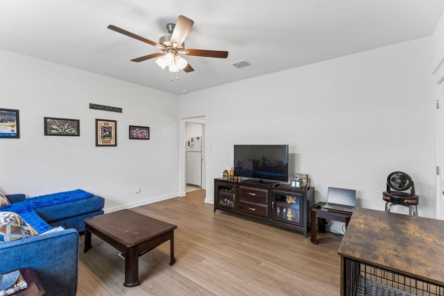 Spacious living area featuring light wood-finish flooring, a contemporary ceiling fan with integrated lighting, and crisp white walls