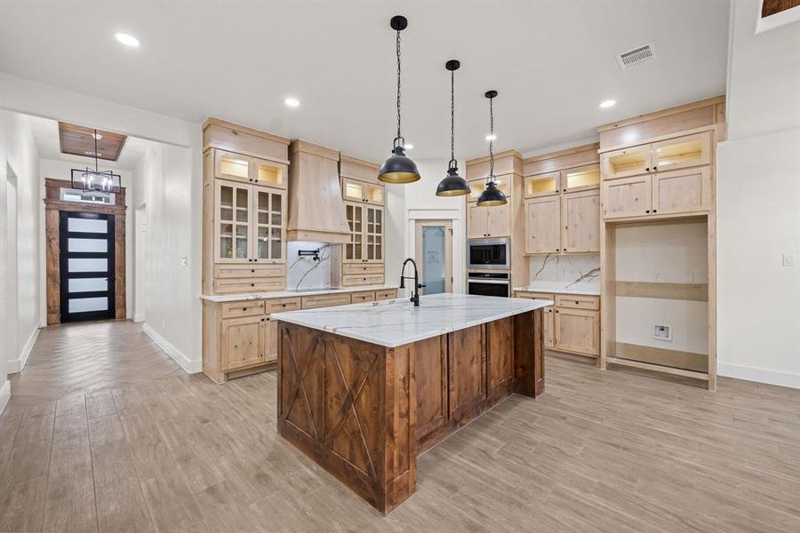 Kitchen with light brown cabinetry, glass insert cabinets, tasteful backsplash, hanging light fixtures, and recessed lighting