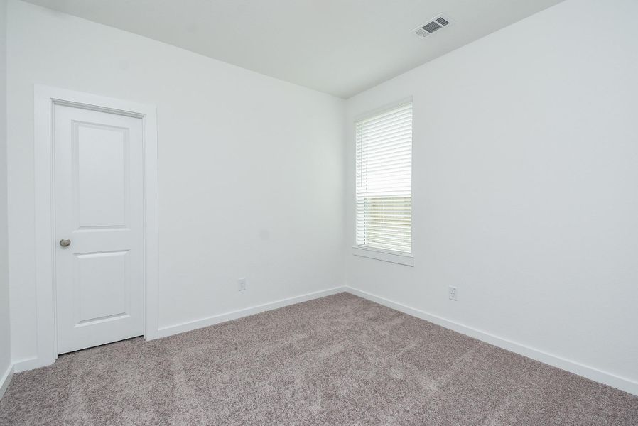 A corner window in a spacious carpeted secondary bedroom gives you more wall/floor space.
