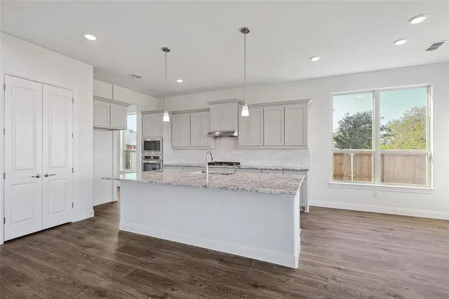 Kitchen with gray cabinets, light stone counters, hanging light fixtures, dark hardwood / wood-style floors, and appliances with stainless steel finishes