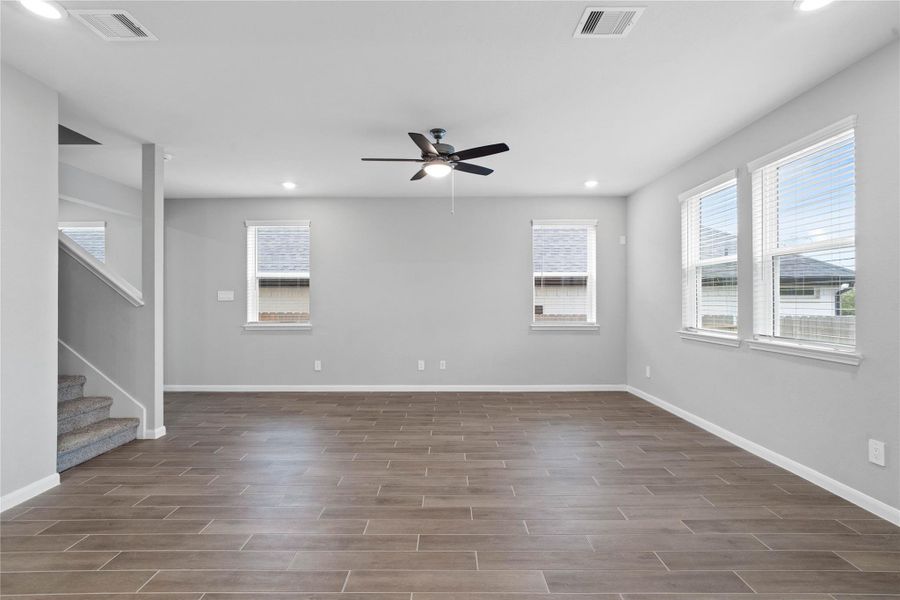A bright and airy open-concept space featuring wood-look tile flooring, high ceilings with recessed lighting and ceiling fan, and abundant natural light from large windows (fitted with blinds).