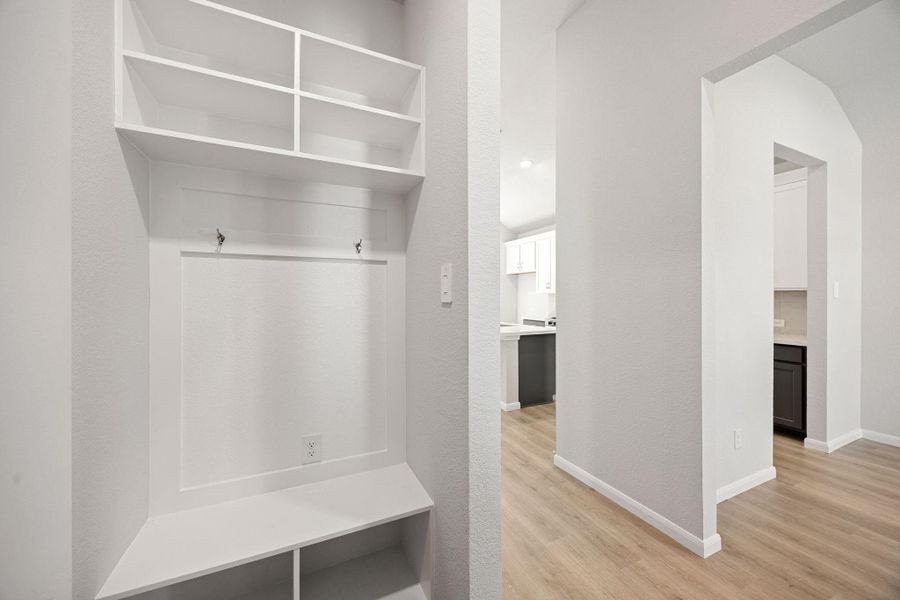 An efficient and organized mudroom or drop zone located off the main hallway, featuring built-in white storage cubbies, a bench for seating, upper shelving, and coat hooks for optimal functionality and organization. An efficient and organized mudroom or drop zone located off the main hallway, featuring built-in white storage cubbies, a bench for seating, upper shelving, and coat hooks for optimal functionality and organization.