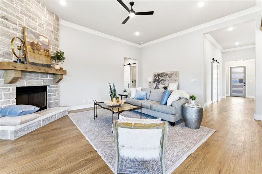 Living room featuring a barn door, crown molding, light wood-type flooring, a stone fireplace, and ceiling fan