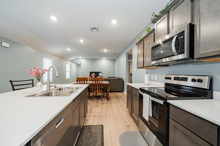Kitchen with stainless steel appliances, dark brown cabinets, light wood-style floors, recessed lighting, and open floor plan Kitchen with stainless steel appliances, dark brown cabinets, light wood-style floors, recessed lighting, and open floor plan